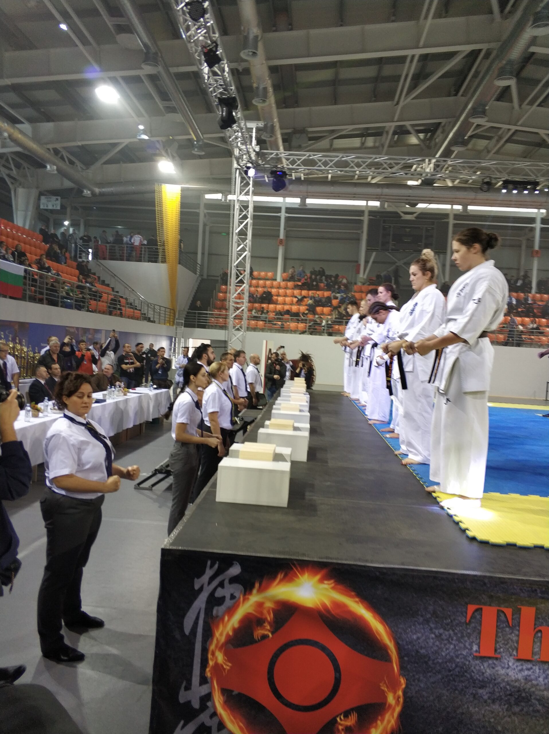 Lângă ei — un șir de judecători în cămăși albe și mesele secretariatului Ceremonia de deschidere a Al 17-lea campionat european deschis de karate: sportivii în kimono pe scena arenei